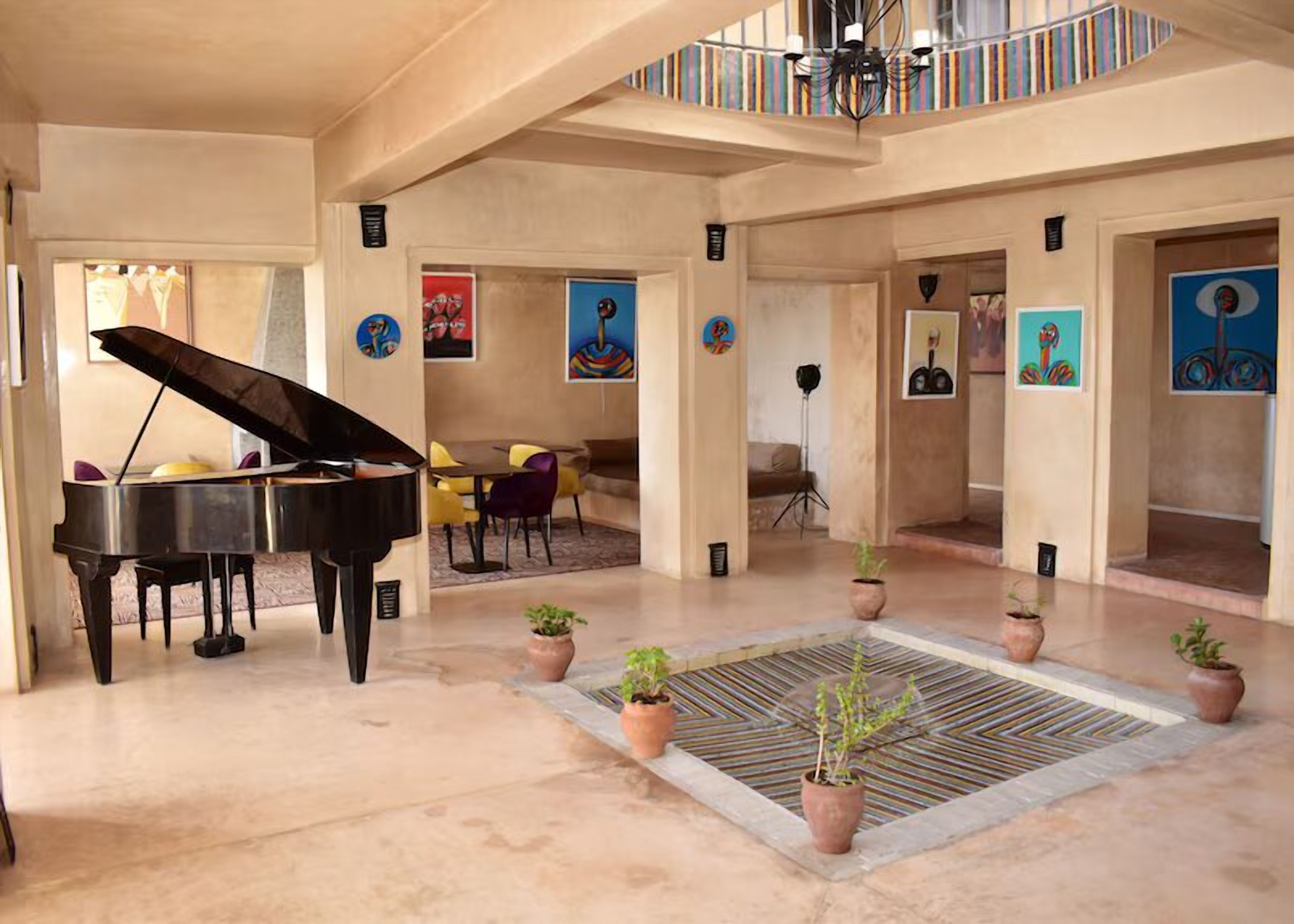 Un piano à queue dans une salle basse de riad, murs de tadelakt, toiles colorées et bassin de mosaïque