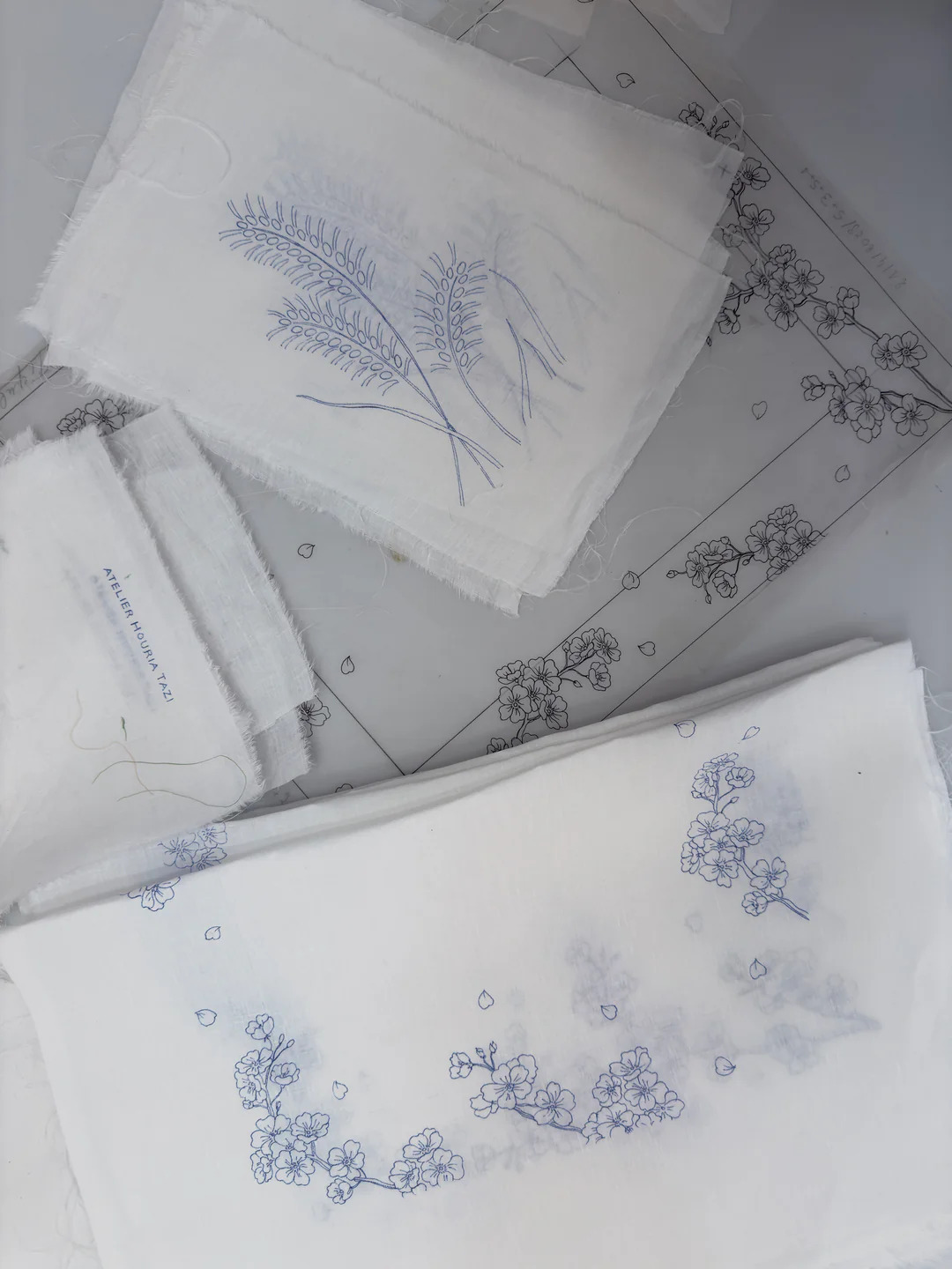 Croquis de fleurs de cerisier reportés au crayon bleu sur des carrés de lin, prêts à broder