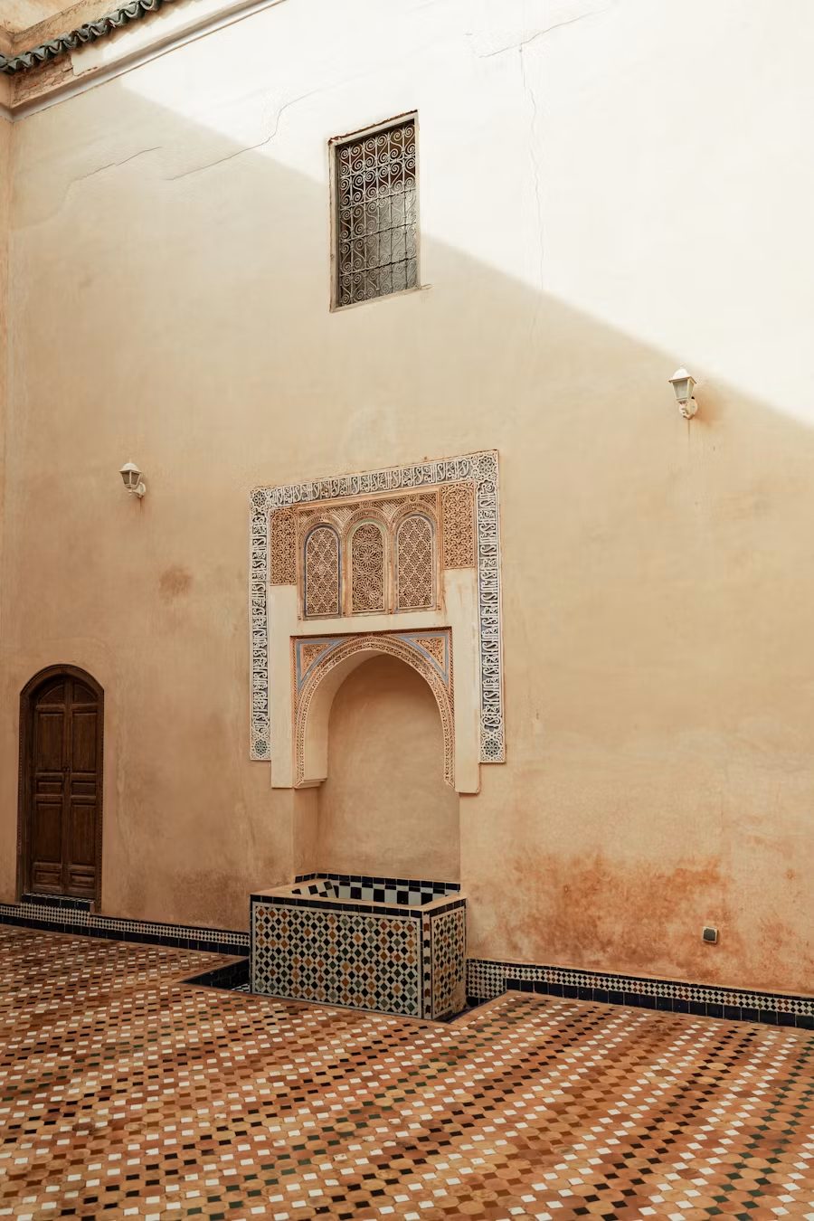 Cour marocaine, niche sculptée et panneaux de zellige sur un mur ocre