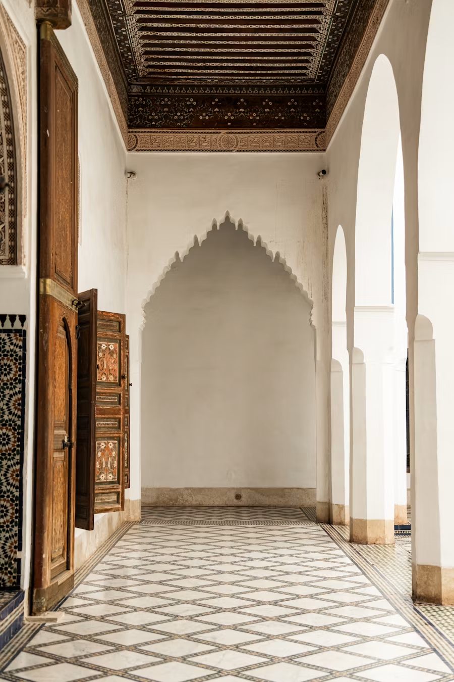 Galerie à arches marocaines, portes de bois sculpté et sol de zellige